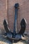 Huge vintage black metal anchor with two large pointed paws standing on the ground, propped up and attached to a red brick wall