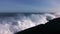 Huge waves crashing against the rocks and releasing large amounts of white foam