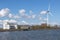 Huge windmill, a farm, a white building on the shore of the dike by the sea with bare trees in the background