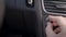 Human is adjusting volume of radio inside car, rotating handle on control panel, close-up of hand