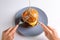 A human cuts a homemade cheeseburger with cutlery with a knife and fork on a gray plate on a white background. Hands in