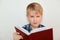 Human face expressions and emotions. Children and education. A close-up of attractive little boy with fair hair reading a book bei