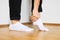 Human feet putting on white ankle socks by hand standing on wooden floor