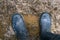 Human feet in rubber boots stand in the mud