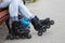 Human feet are wearing in-line skates. Woman and kid sitting on bench while rollerblading