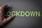 Human fingers holding the word Lockdown written with plastic letters on brown paper background