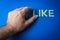 Human fingers picking the word Like written with plastic letters on blue paper background