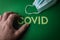 Human fingers removing the word Covid written with plastic letters on green paper background