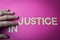 Human fingers sliding two letters to the word Injustice to make it Justice, written with plastic letters on a bright pink paper ba