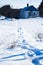 Human footprints in the snow, winter path in the field leading to the small rural house