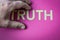 Human hand hiding the word Truth written with plastic letters on a bright pink paper background