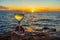 Human hand holding wine glass with sparkling wine against amazing sea landscape at sunset. Beautiful still life with alcohol drink
