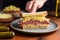 human hand placing a pickle beside a reuben sandwich on a plate