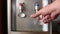 Human hand pouring cold water in glass from water dispenser.