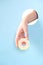 Human hand protruding through hole in blue background, holding donut