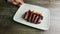 Human hand rotates modern plate with sliced meat and garnish