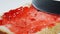 Human hand smears a cherry jam on a bread slice