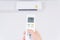 Human hand is using white remote of air conditioner for turn on or adjust temperature of air conditioner inside the room