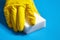 Human hand in yellow glove holds a white melamine sponge on blue