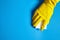 Human hand in yellow glove holds a white melamine sponge on blue background with copy space