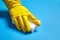 Human hand in yellow rubber glove holds a white melamine household sponge on blue