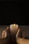 Human hands, cylindrical candle against dark background.Empty space.Vertical image