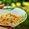 Human hands hold a bowl with pilau on a blurred background of gr