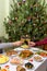 Human hands holding glasses with sparkling wine against beautiful decorated Christmas tree and served table with tasty dishes. New