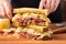 human hands layering slices of meat on a reuben sandwich