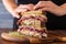 human hands layering slices of meat on a reuben sandwich