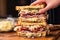 human hands layering slices of meat on a reuben sandwich