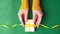Human hands puts white gift box with a yellow satin ribbon bow on jade green background with gold colored glitter. Stop motion