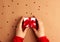 Human hands with red sleeves holding a brown paper gifts with a red satin ribbon bow on brown background with red stars shapes.