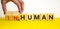 Human or inhuman symbol. Businessman turns wooden cubes and changes the word inhuman to human. Beautiful yellow table white
