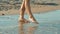 Human legs touching sea water and run away abruptly. Girl feet on sandy beach