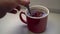 Human's hand pours spoonful of sugar into ceramic mug with tea.