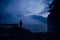 Human silhouette in a blue haze on the background of mountains and river. Thick fog in the evening twilight. Mysterious atmosphere