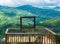 Human Size Wooden Picture Frame on a Platform With Background of A Green Forest and Mountains In A Sunny Clear Blue Sky