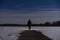 Human standing outdoor at night on ice lake with flashlight and hoodie on head