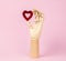 Human wooden hand model with red heart on pastel pink. Heart health concept