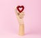 Human wooden hand model with red heart on pastel pink. Heart health concept