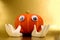 Humanoid pumpkin with plastic eyes and two porcelain hands against a golden background close up.