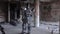 Humanoid robot stands with his back in hat in abandoned building. Footage. Android on date with glasses and bottle of