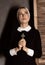 Humble young beautiful nun in robes holding a cross on a grey background