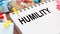 HUMILITY - text on a notepad with wrinkled paper and paper needles on wooden background