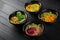 Hummus garnished peppers, chili, beet and herbs in black bowl on dark wooden table. Hummus assortment