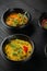 Hummus garnished peppers, chili, beet and herbs in black bowl on dark wooden table. Hummus assortment