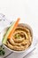 Hummus sauce in a bowl, sesame seeds, olive oil, cucumber and carrots on a light background