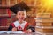 Humorous portrait of very happy beautiful young school girl in graduation cap  making education plan for the future in library