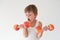 Hungry active strong small child in tank top lifting dumbbells made from apples fruits wishing to bite and eat food